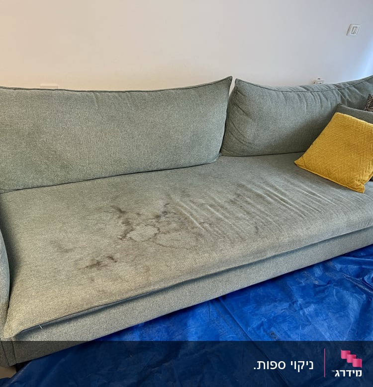 ספה עם כתמים על בד וכיסוי מגן כחול על הרצפה